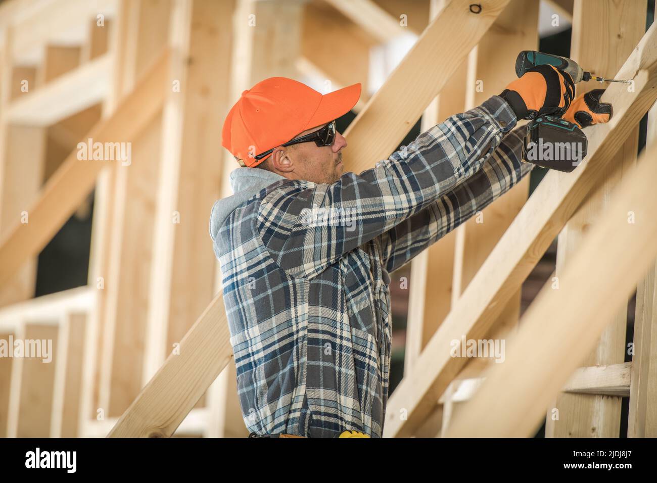 Carpenter Building the Skeleton of a New Wooden Residential House Using Electric Screwdriver to Secure Wooden Frame Beams with Screws. Construction Si Stock Photo