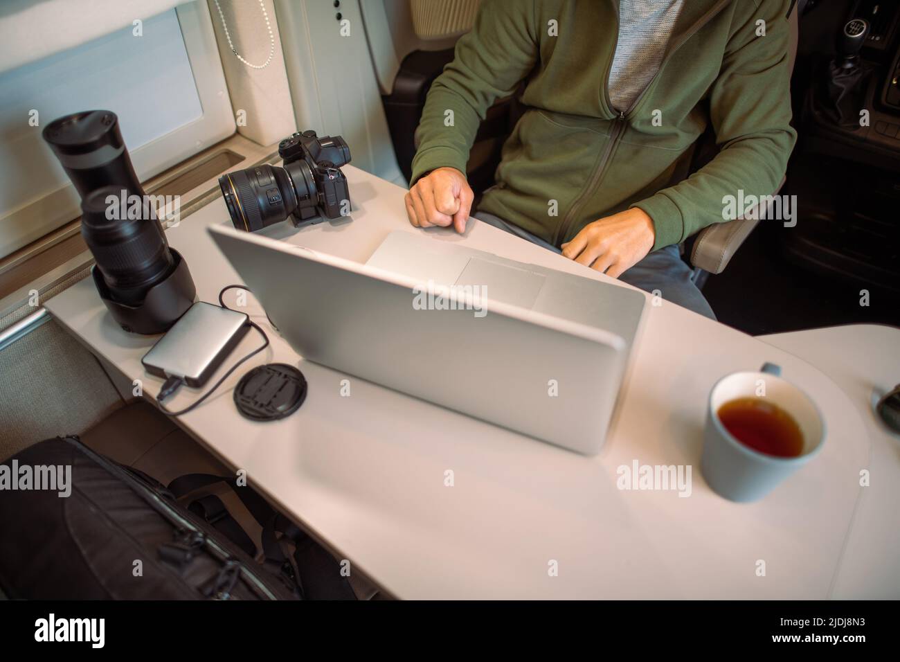 Travel Photographer Transferring His Latest Photos from His Photo Camera to the Laptop Computer Sitting in His Camper Van During the Overnight Stay. Stock Photo
