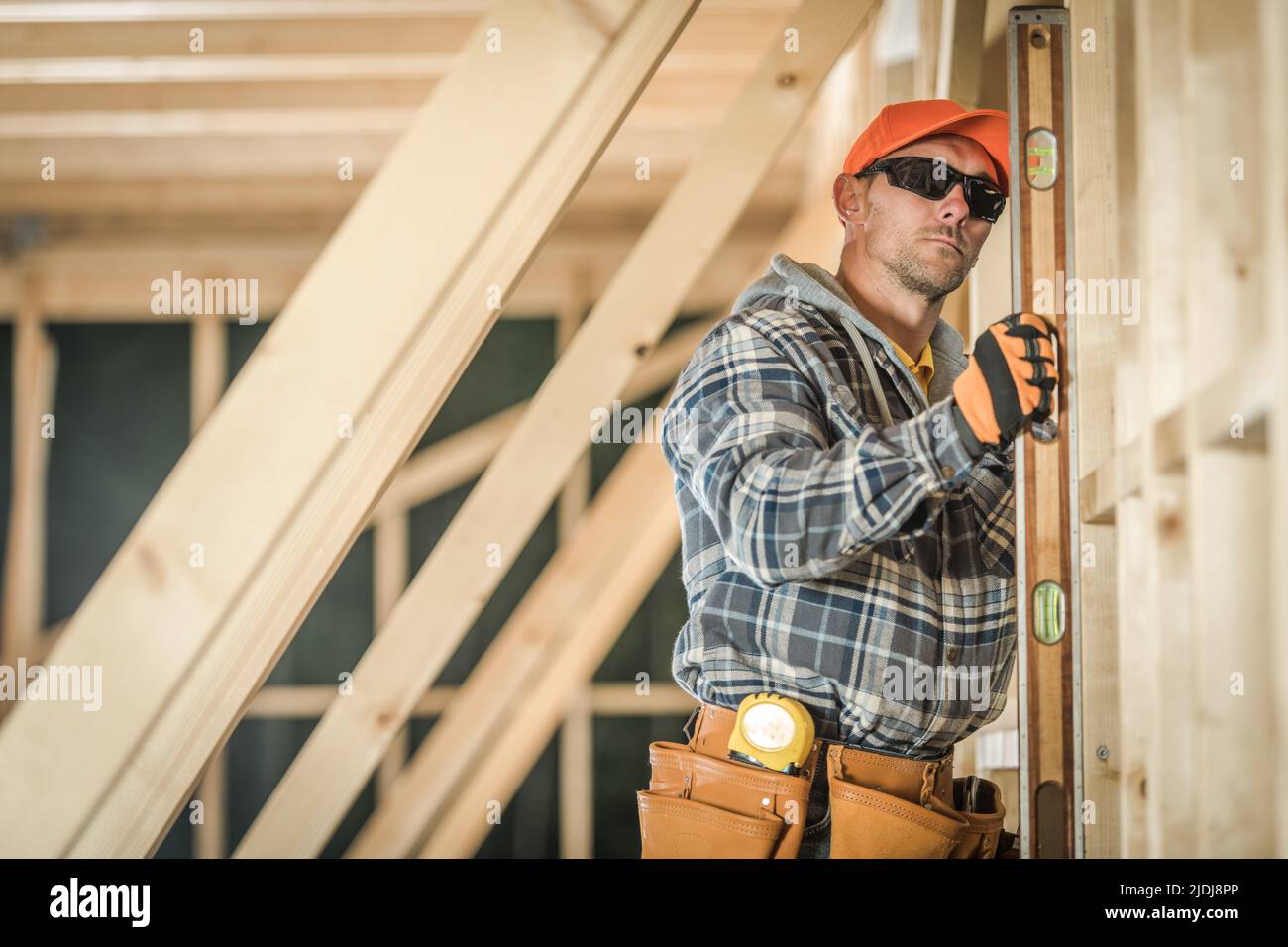 Caucasian Construction Worker Verifying the Straightness of Freshly Built Wooden House Roof Skeleton Using His Building Spirit Level Tool. Constructio Stock Photo