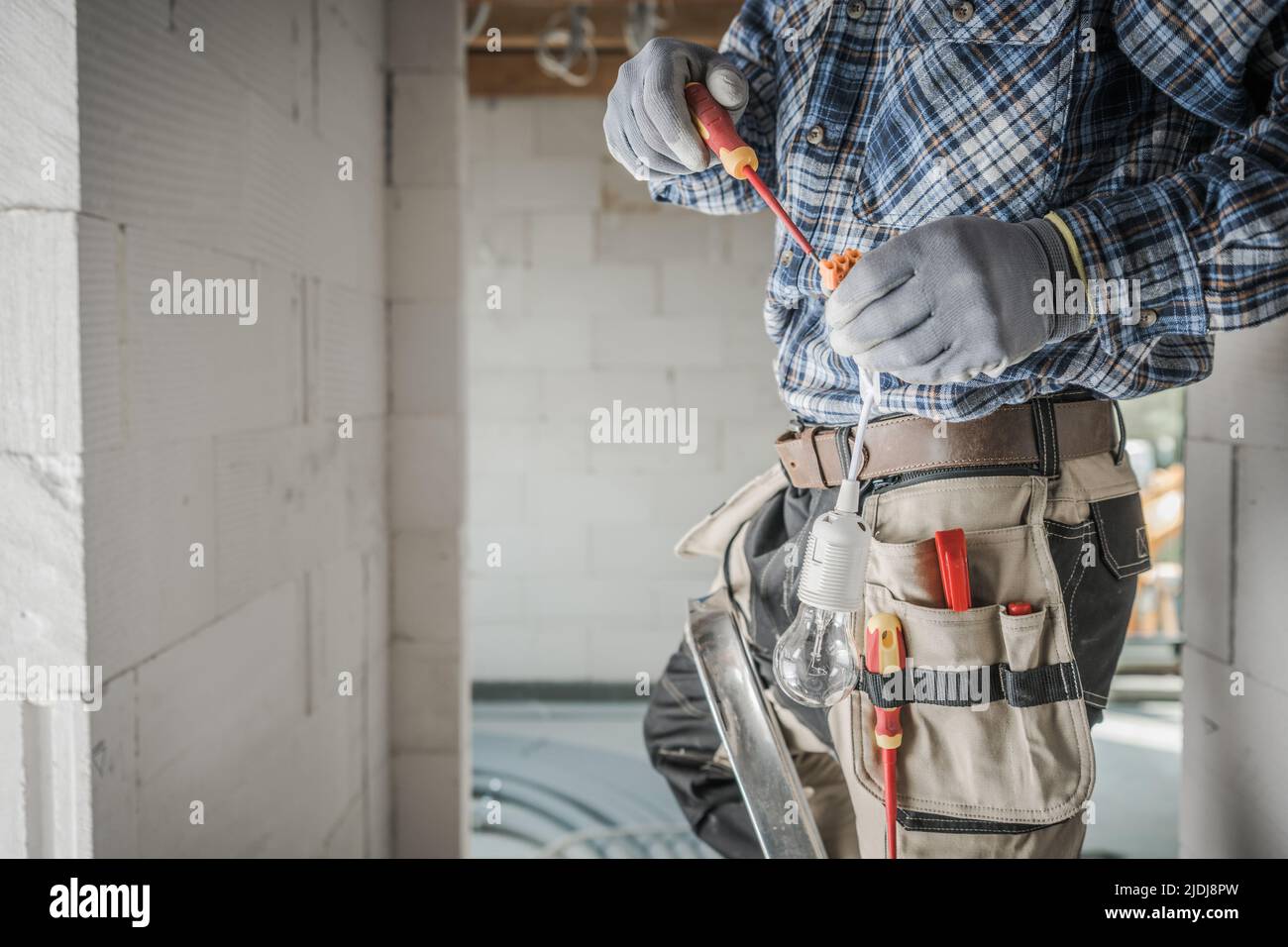 Electrician Contractor in His Tool Belt Installing Lightning in the Newly Built Residential Building. Professional Worker. Construction and Electricit Stock Photo