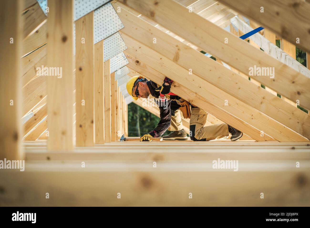 Building Process of the Roof Wooden Skeleton in the New Residential House. Caucasian Worker Driving the Nails Into Beams Using His Claw Hammer Constru Stock Photo