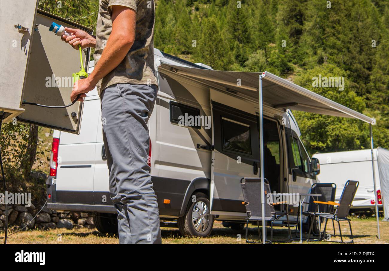 Caucasian Men in His 40s Connecting His Camper Van to RV Park Electric Power Outlet. Vacation Traveling in a Motorhome. Stock Photo
