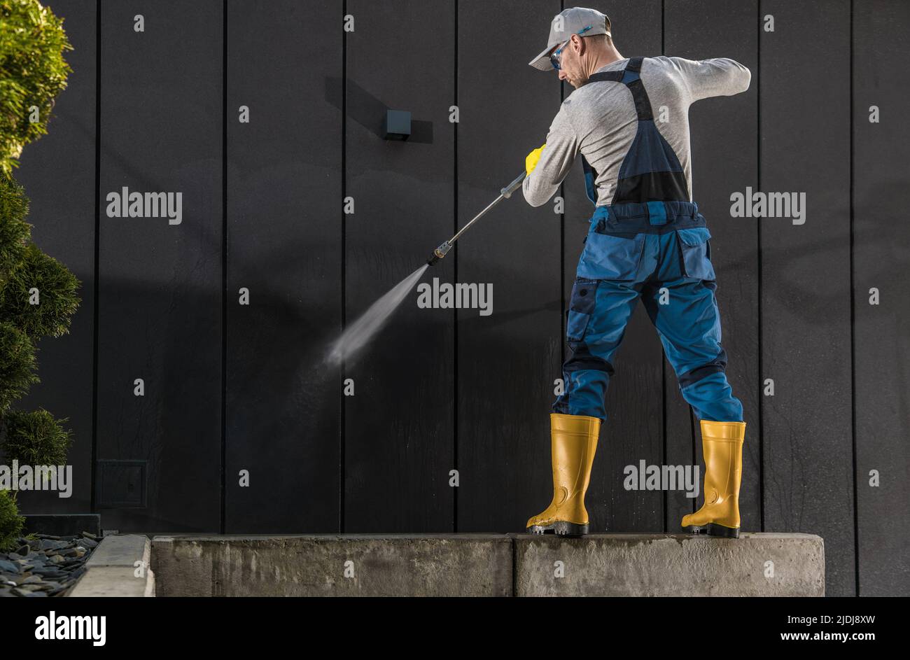 Caucasian Worker in His 40s Cleaning Modern Building Dark Wall Using Powerful Pressure Washer Stock Photo