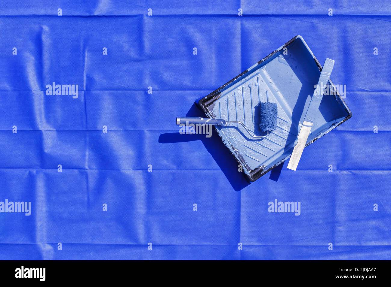 Paint tray and roller with stir stick on blue drop cloth Stock Photo
