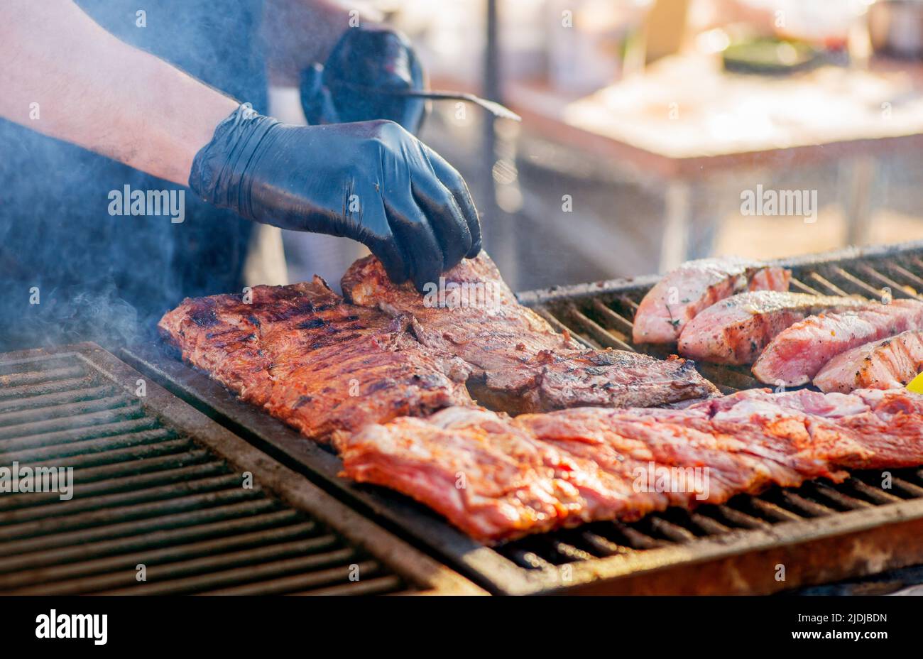 Barbecue ribs. Man in gloves flips grilled ribs on a charcoal grill
