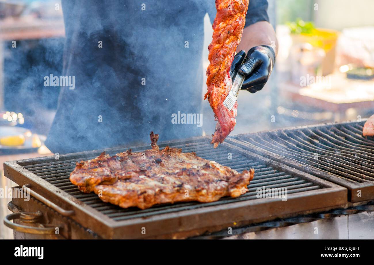 Barbecue ribs. Man in gloves flips grilled ribs on a charcoal grill