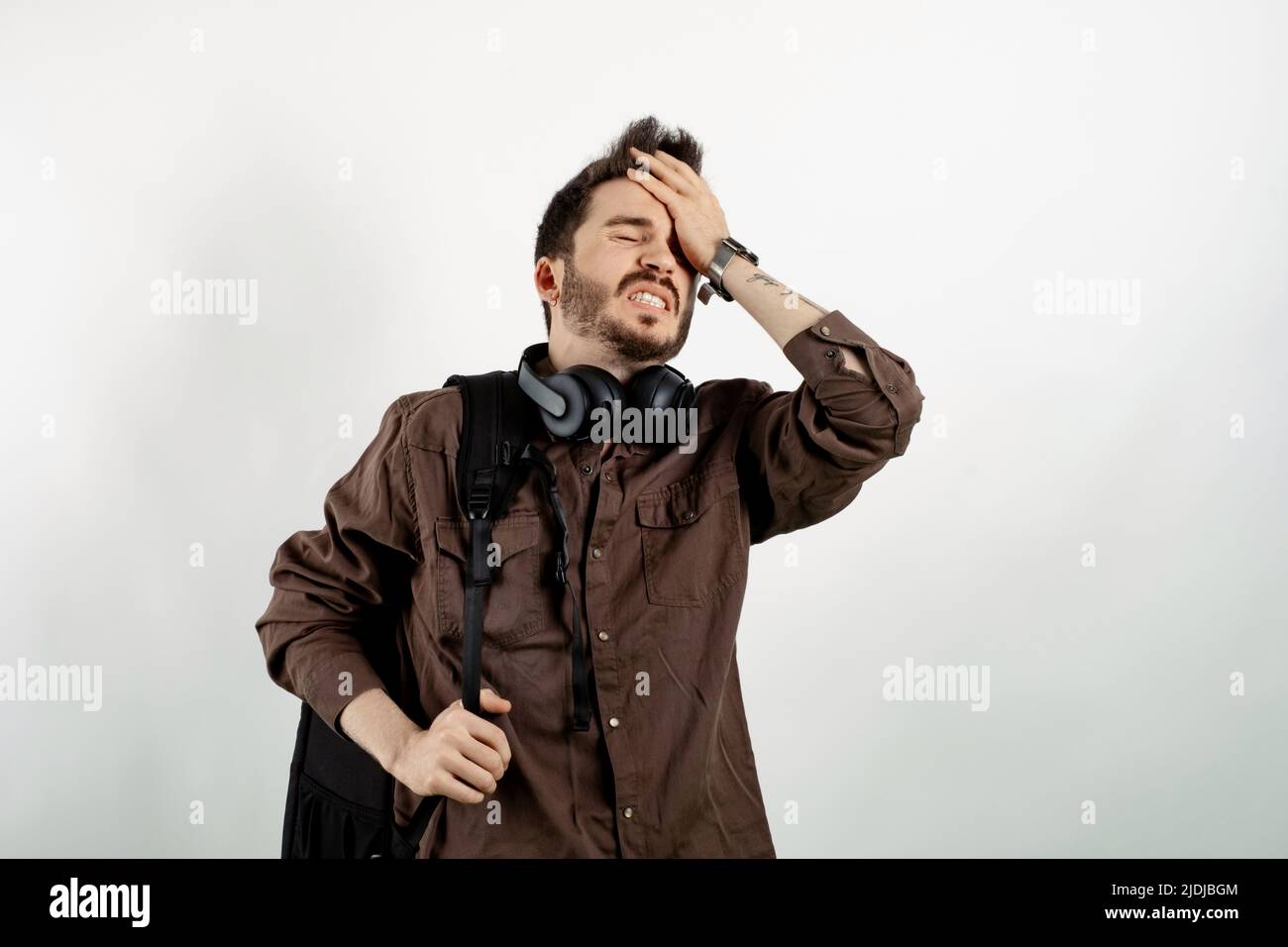 Portrait of man wearing brown shirt posing isolated over white background suffering headache and holding hands on forehead. Education in university co Stock Photo
