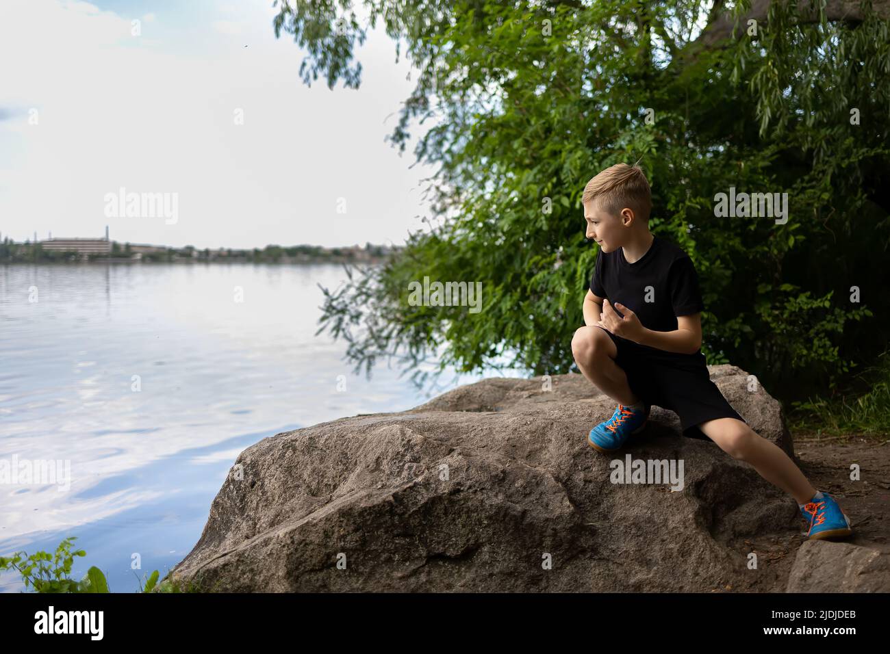 a boy looks into the river sitting on a stone Stock Photo - Alamy