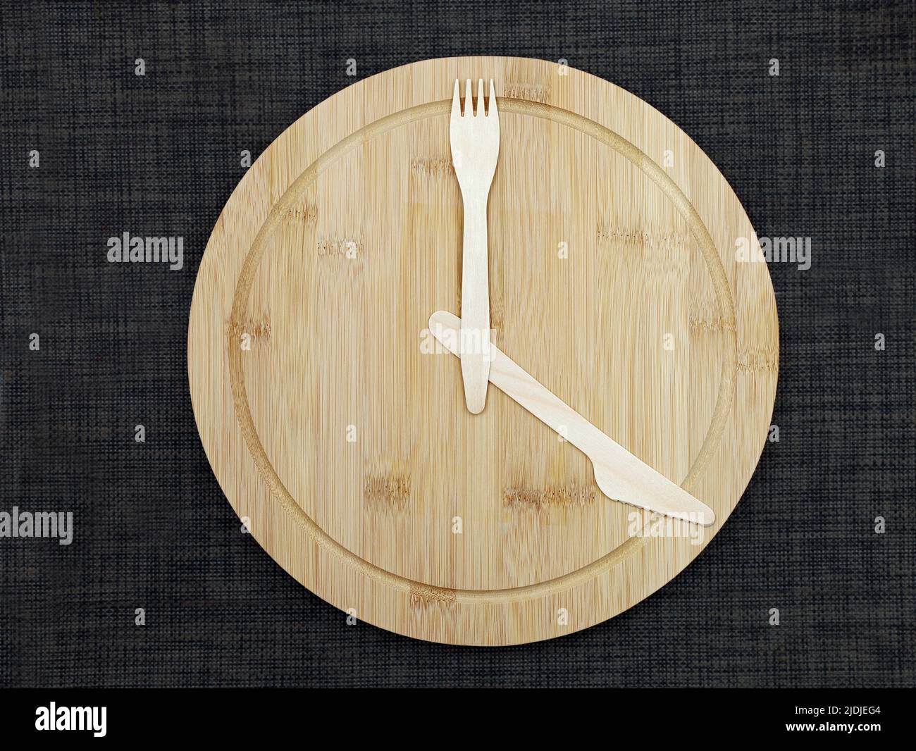 wooden fork and knife as clook hands on bamboo plate shows time, concept of intermittent fasting or time limited food intake to lose weight Stock Photo