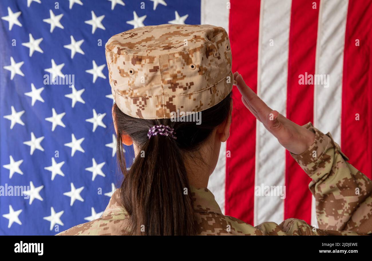 Female US Army Soldier standing in front of an American flag and saluting. Woman in military uniform rear view Stock Photo