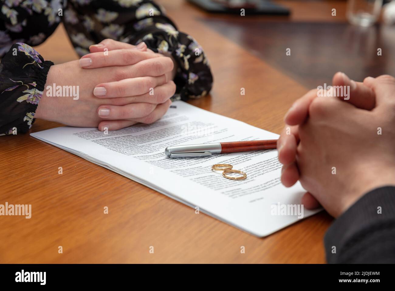 Signing a divorce, marriage dissolution documents and agreement. Wife and husband hands, wedding rings and legal papers for signature on a wooden tabl Stock Photo