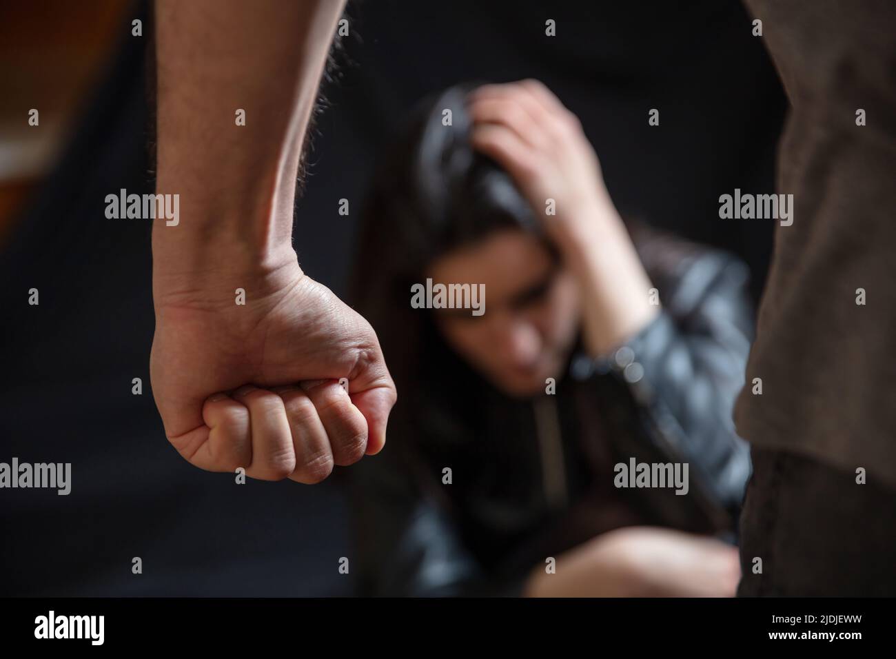 Woman abuse, Young woman scared holding head with hands, male clenched fist close up. Domestic violence, husband against wife. Dark room background Stock Photo