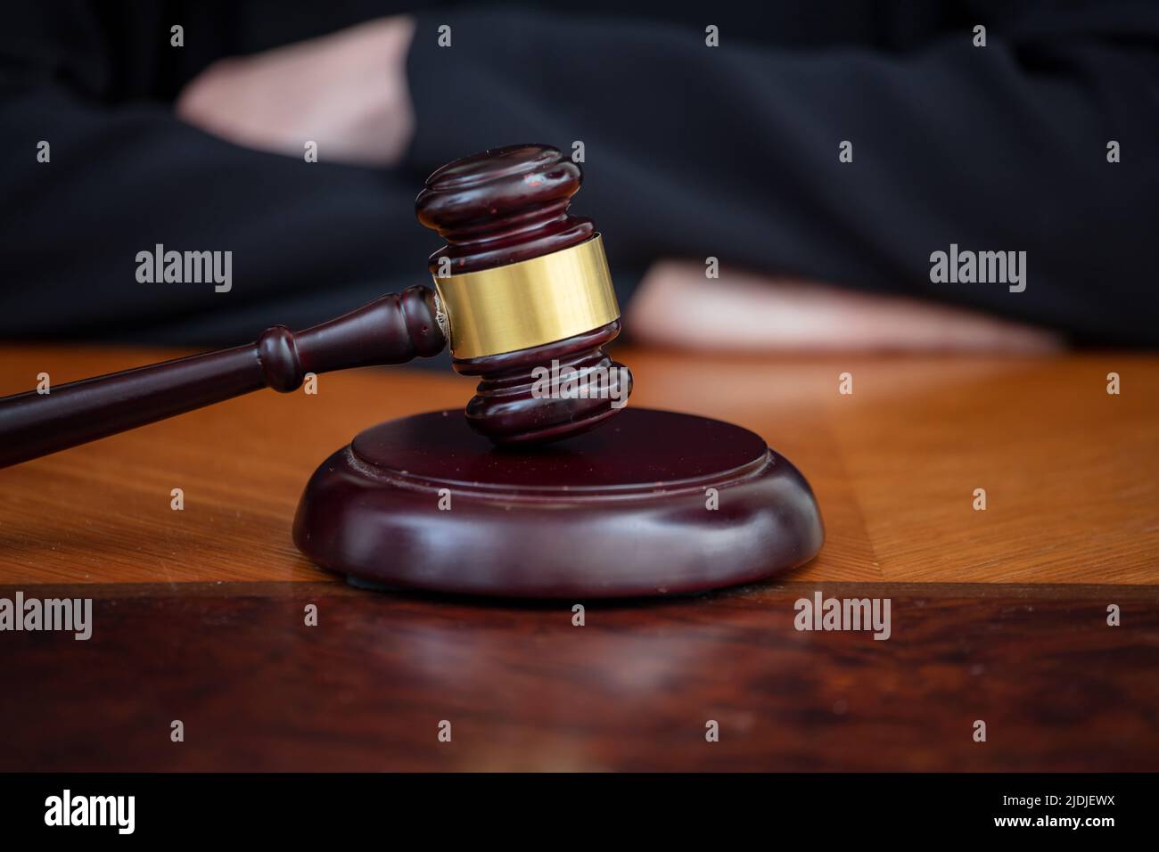 Judge gavel on wooden court desk, blur female crossed hands, close up view. Justice and law concept, lawyer office. Stock Photo