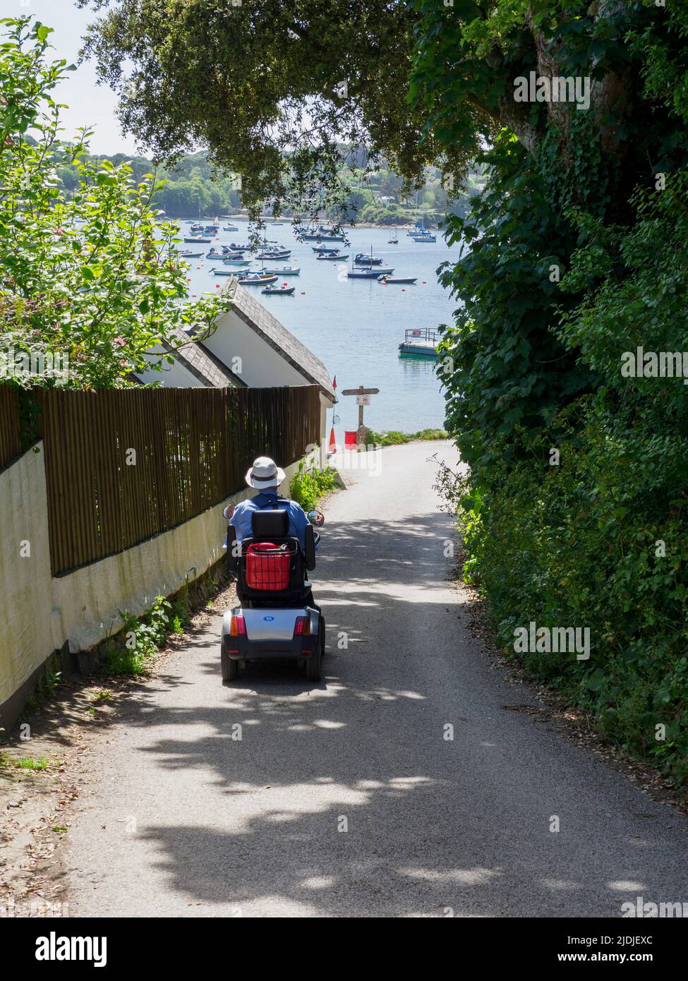 Senior citizen riding a mobility scooter down the road to the beach, Helford Passage, Cornwall, UK Stock Photo