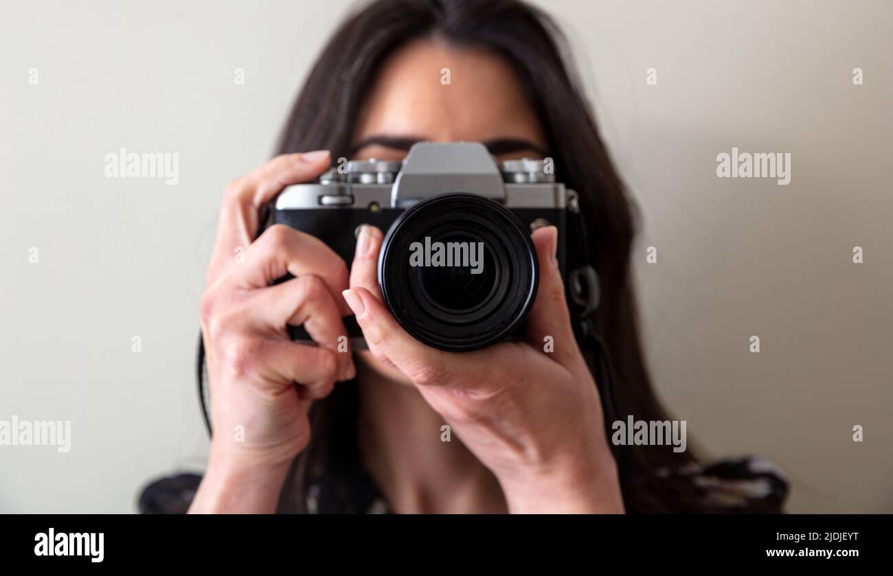 Young woman holding photo camera is shooting your picture. Girl photographer focus at you, close up view Stock Photo