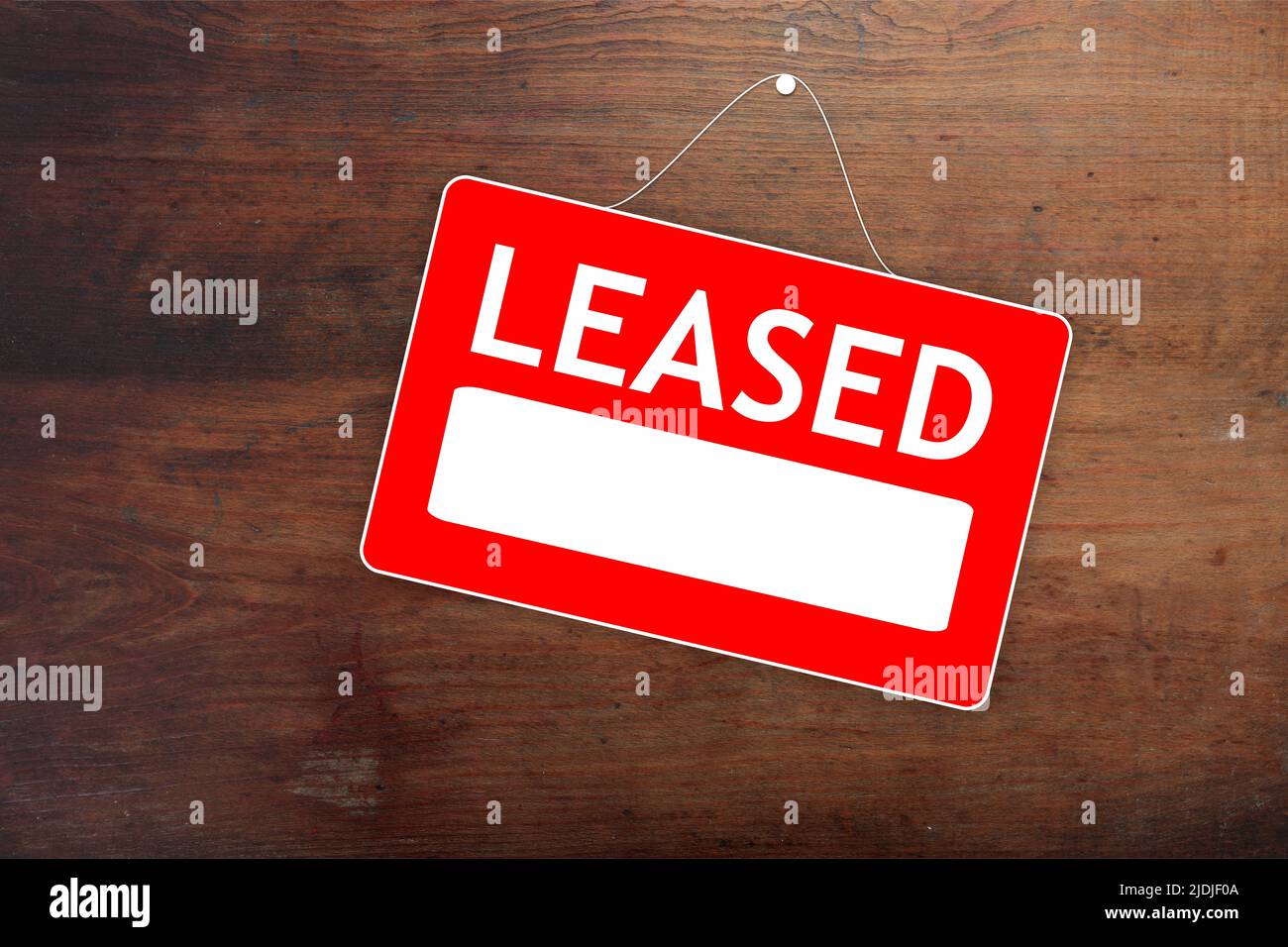 LEASED red sign with white word and empty space for text, advertising template. Label for hired real estate on old wood surface, agreement with agent. Stock Photo