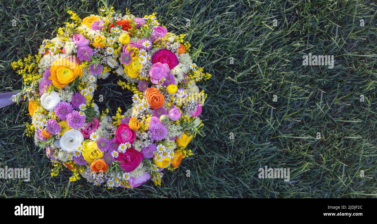 Flower wreath on green grass. Fresh wild flowers and herbs on garden lawn, top view. Spring day. Women or Mothers day celebration, copy space Stock Photo