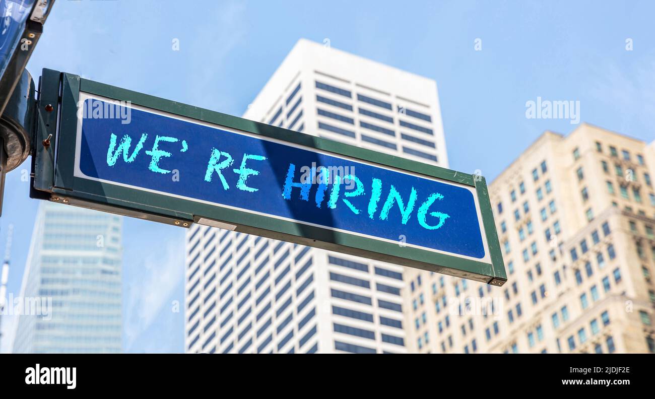 We Are Hiring blue sign in front of skyscraper at city background. We need you at our company concept. Business vacancy text message, advertise, staff Stock Photo