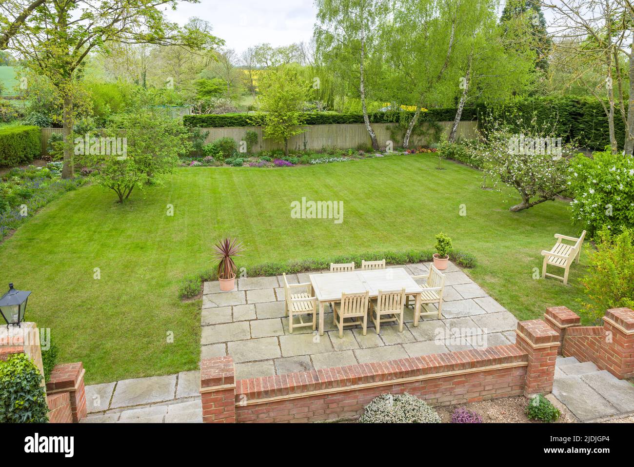 Wooden garden furniture on a patio terrace in a UK landscaped back garden with large lawn Stock Photo