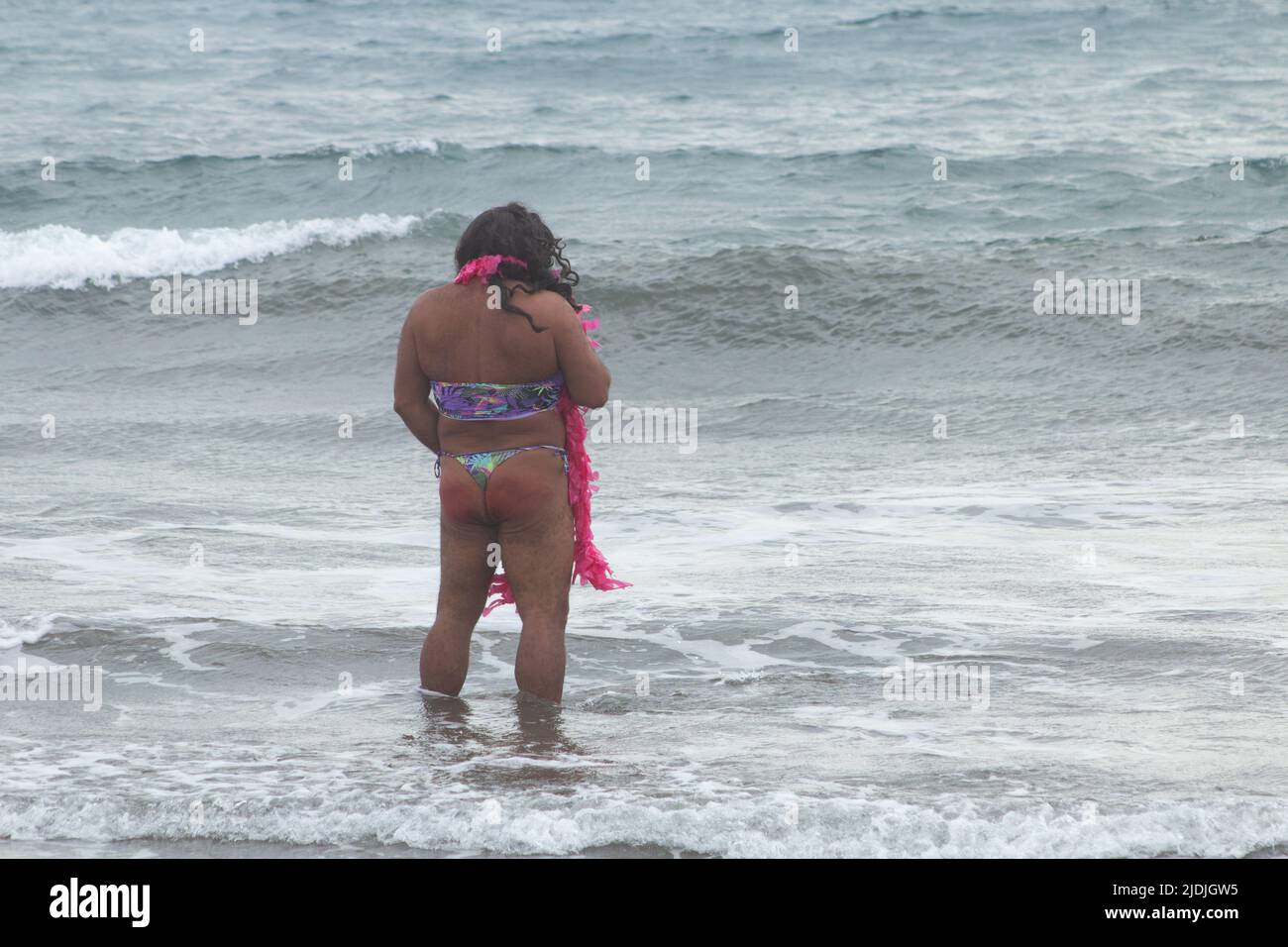 Rear view of man in fancy dress urinating in the sea in Spain Stock Photo