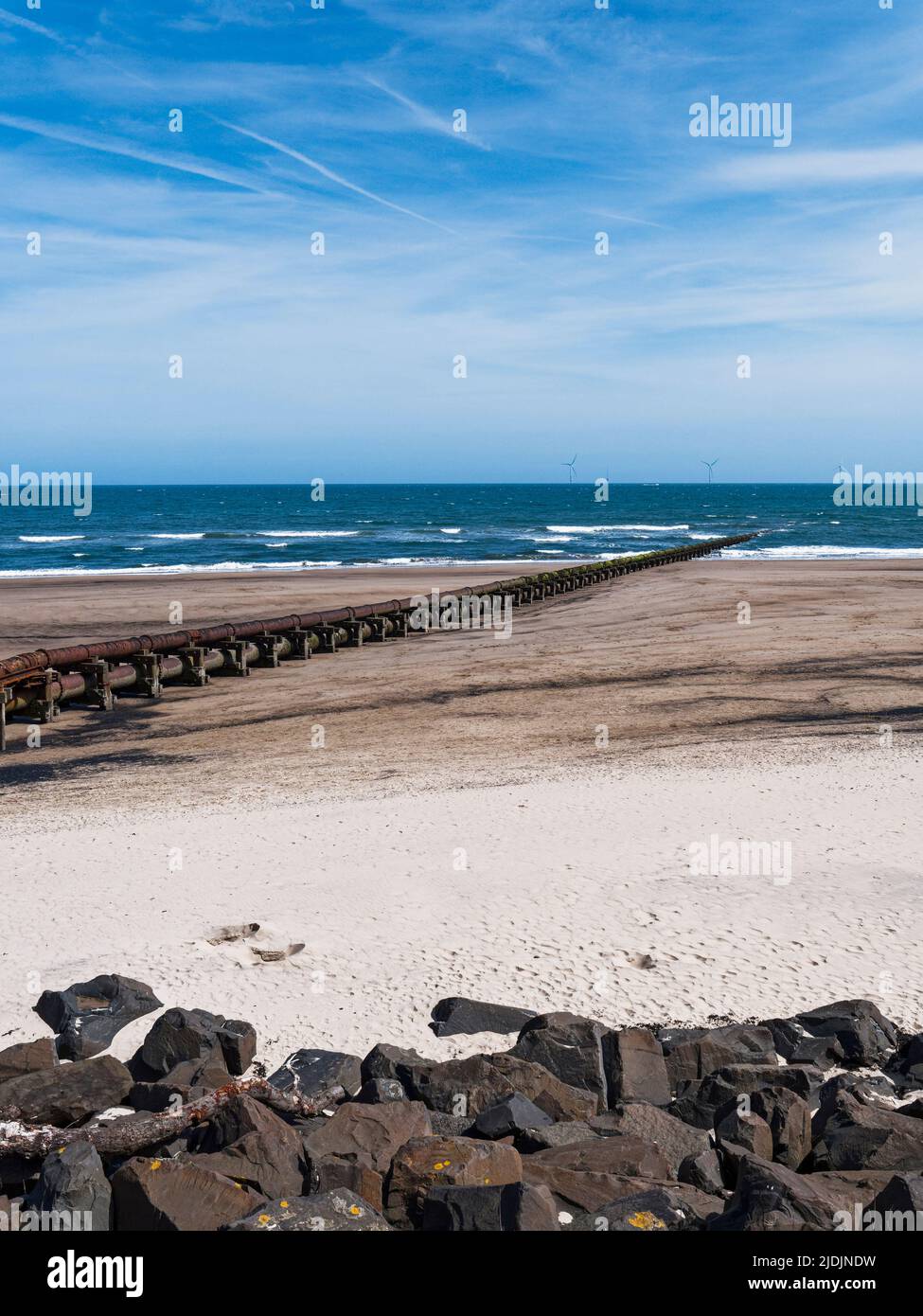 Cambois beach with rocks to prevent erosion and old sewage pipeline and wind turbines. Stock Photo