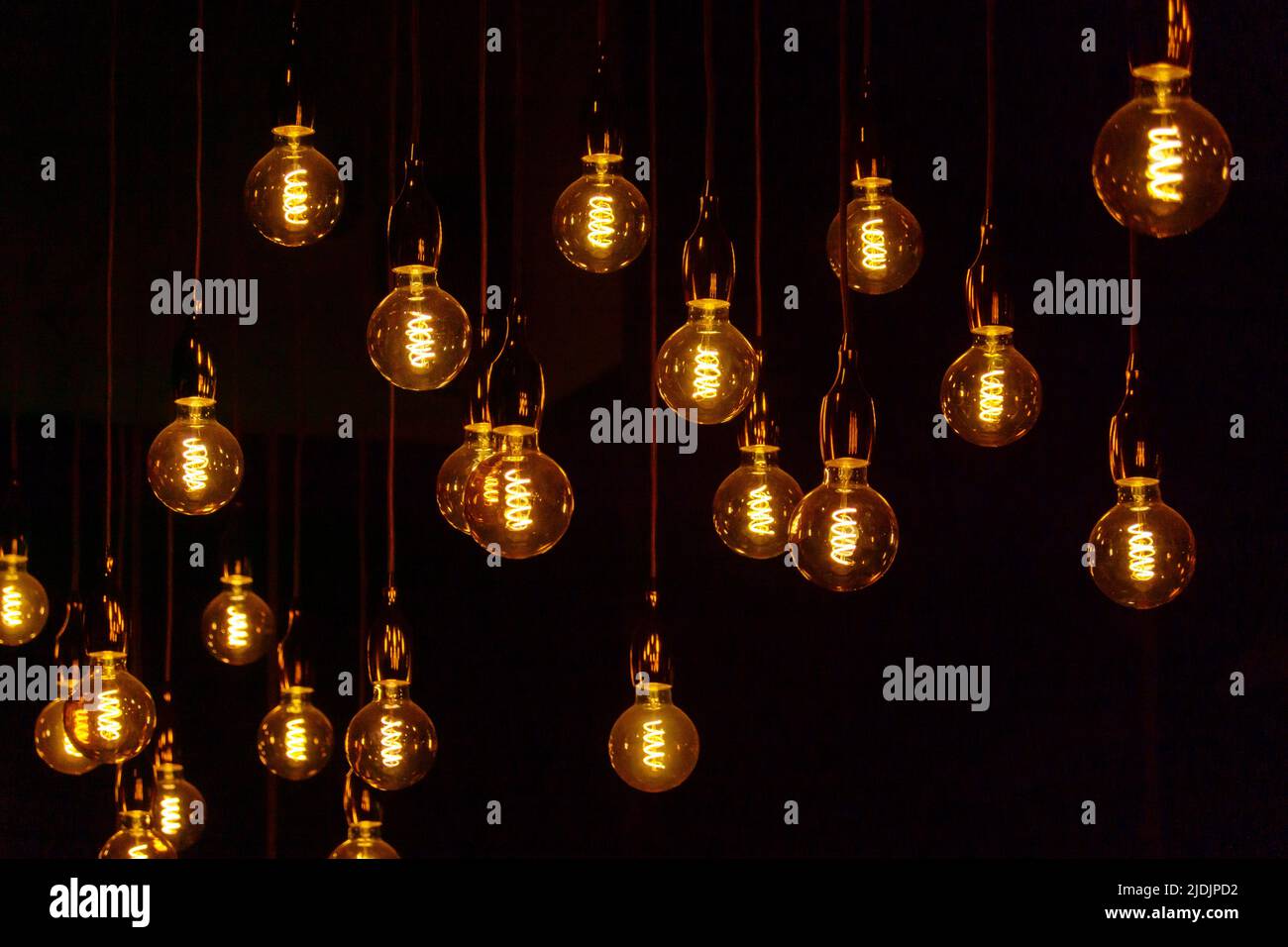 Many vintage light bulbs hanging on cords and glowing against black background at night Stock Photo