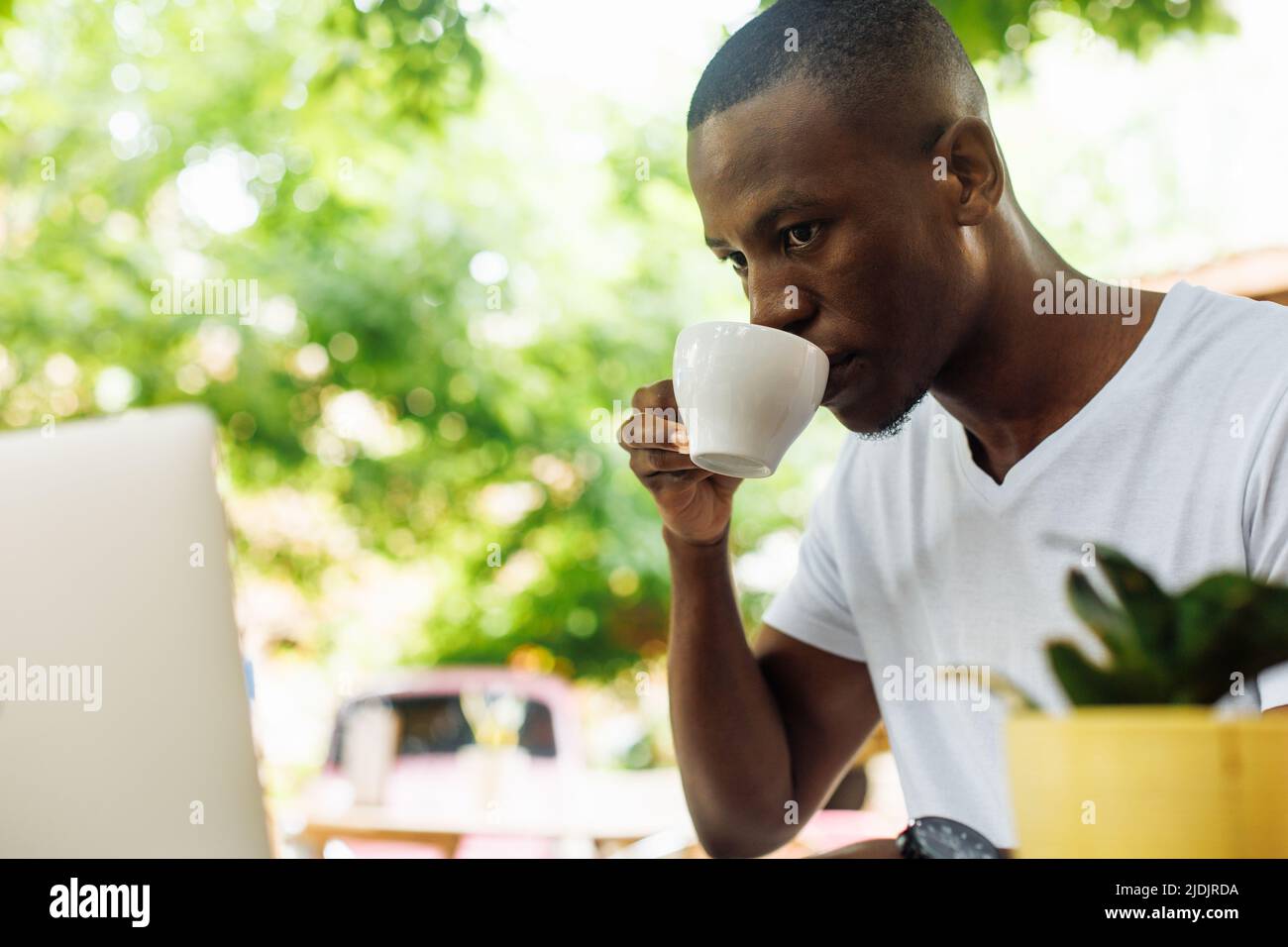 Confident and successful multiracial businessman drinking coffee and work, chatting online using laptop in street cafe Stock Photo