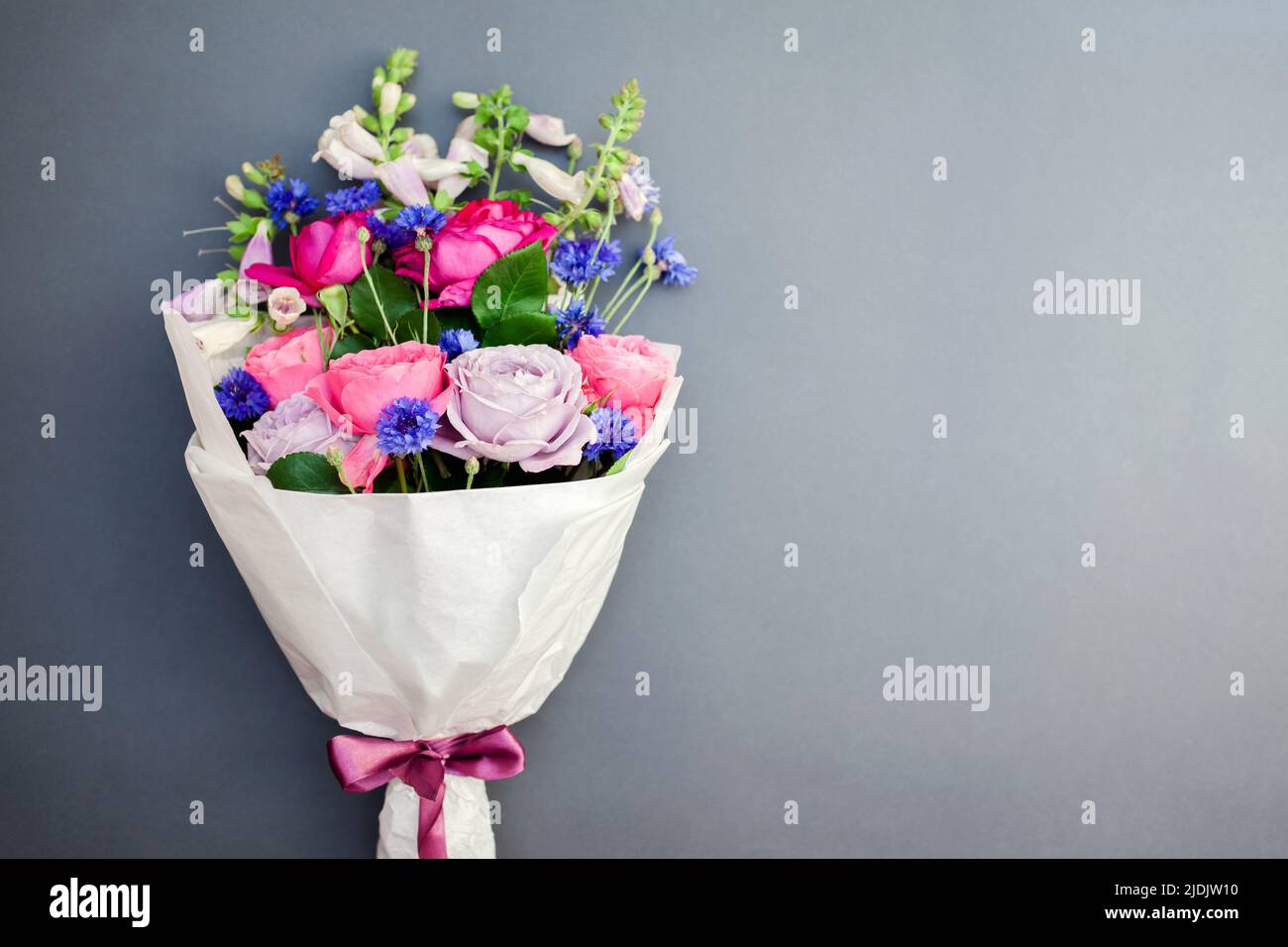 Fresh bouquet of roses foxgloves bachelor buttons flowers wrapped in paper and arranged on background tied with ribbon. Top view. Space Stock Photo