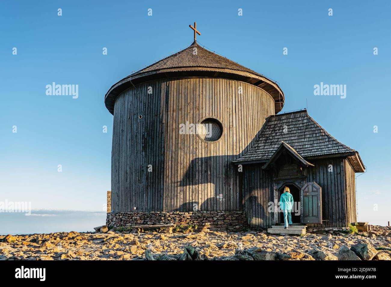 Old wooden church on the top of Snezka,the highest mountain of Czech Republic,Krkonose Mountains. Girl in blue jacket walking to chapel of Saint Lawre Stock Photo