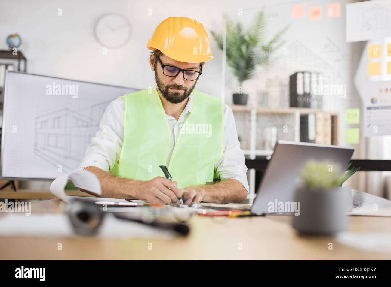 Architect man or male builder hold pen and ruler, writing and drawing architectural project, work on laptop computer on the desk at workplace. Stock Photo