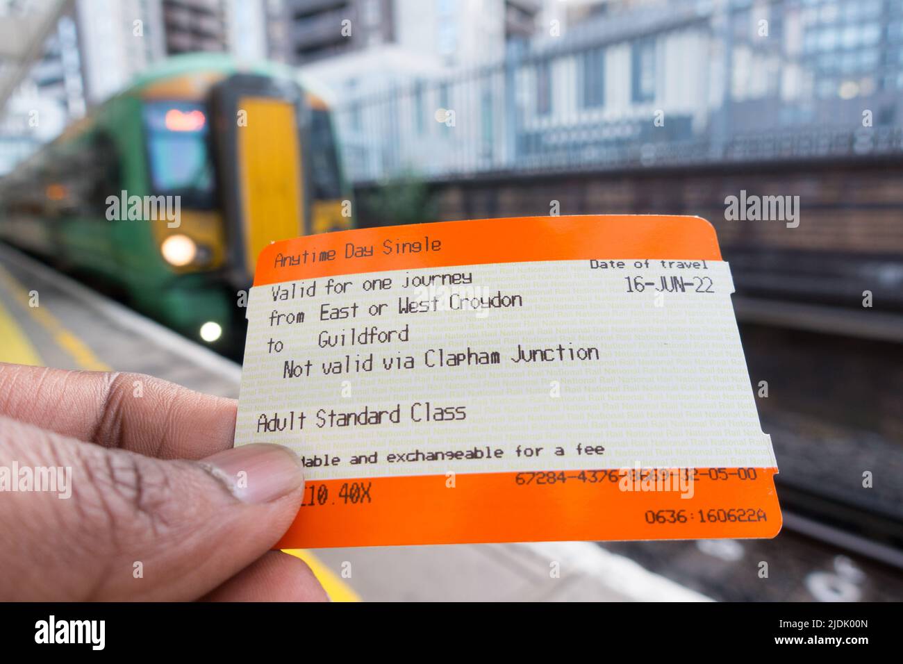 Adult male hand holding a UK train ticket with Train in background Stock Photo