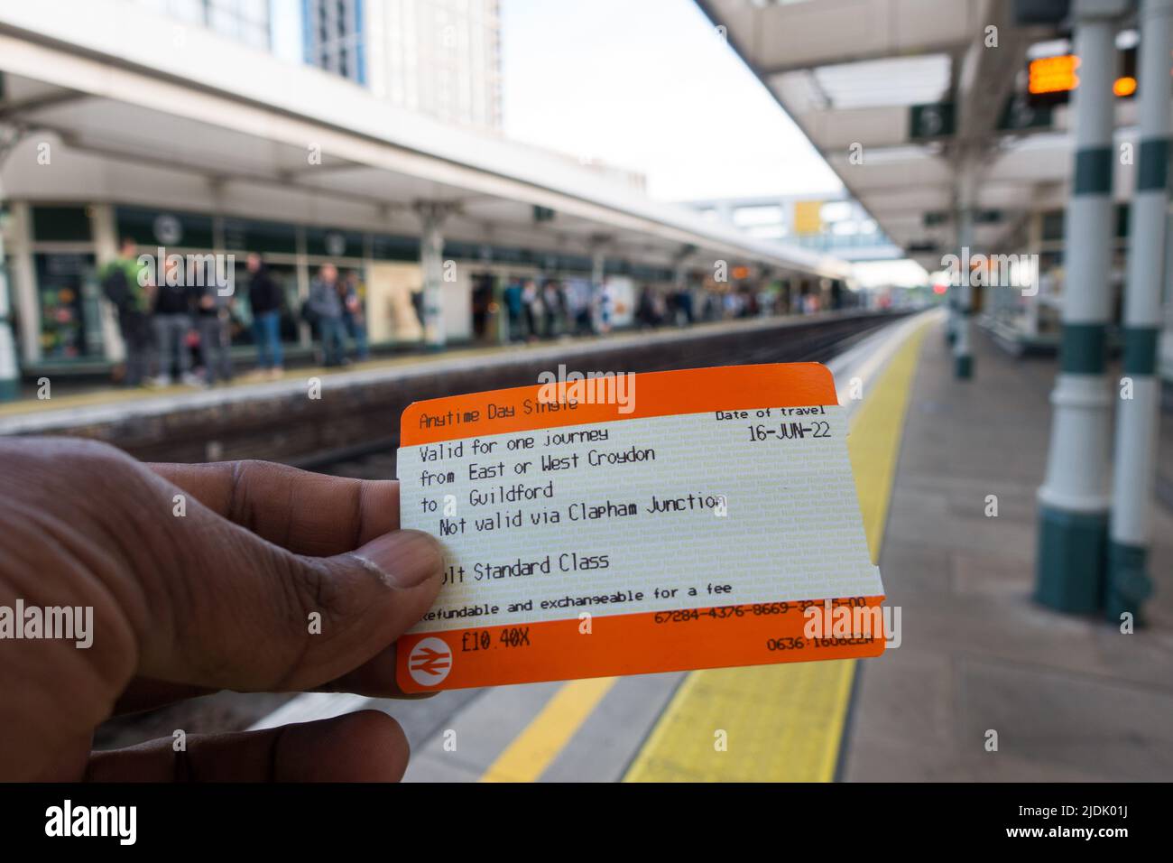 Adult male hand holding a UK train ticket with Train station in background destined for Guildford Stock Photo