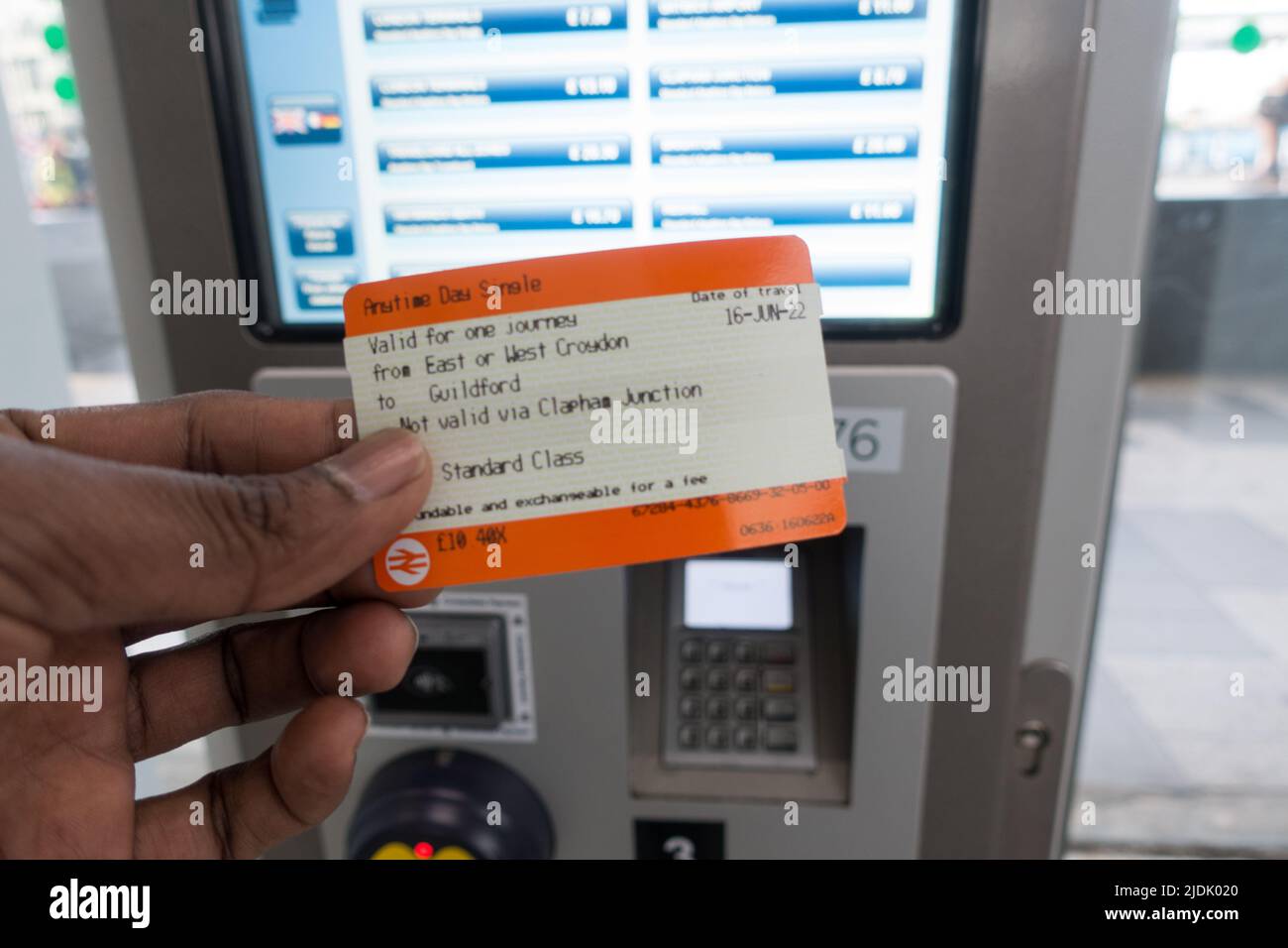 Adult male hand holding a UK train ticket with Train ticket machine in background Stock Photo