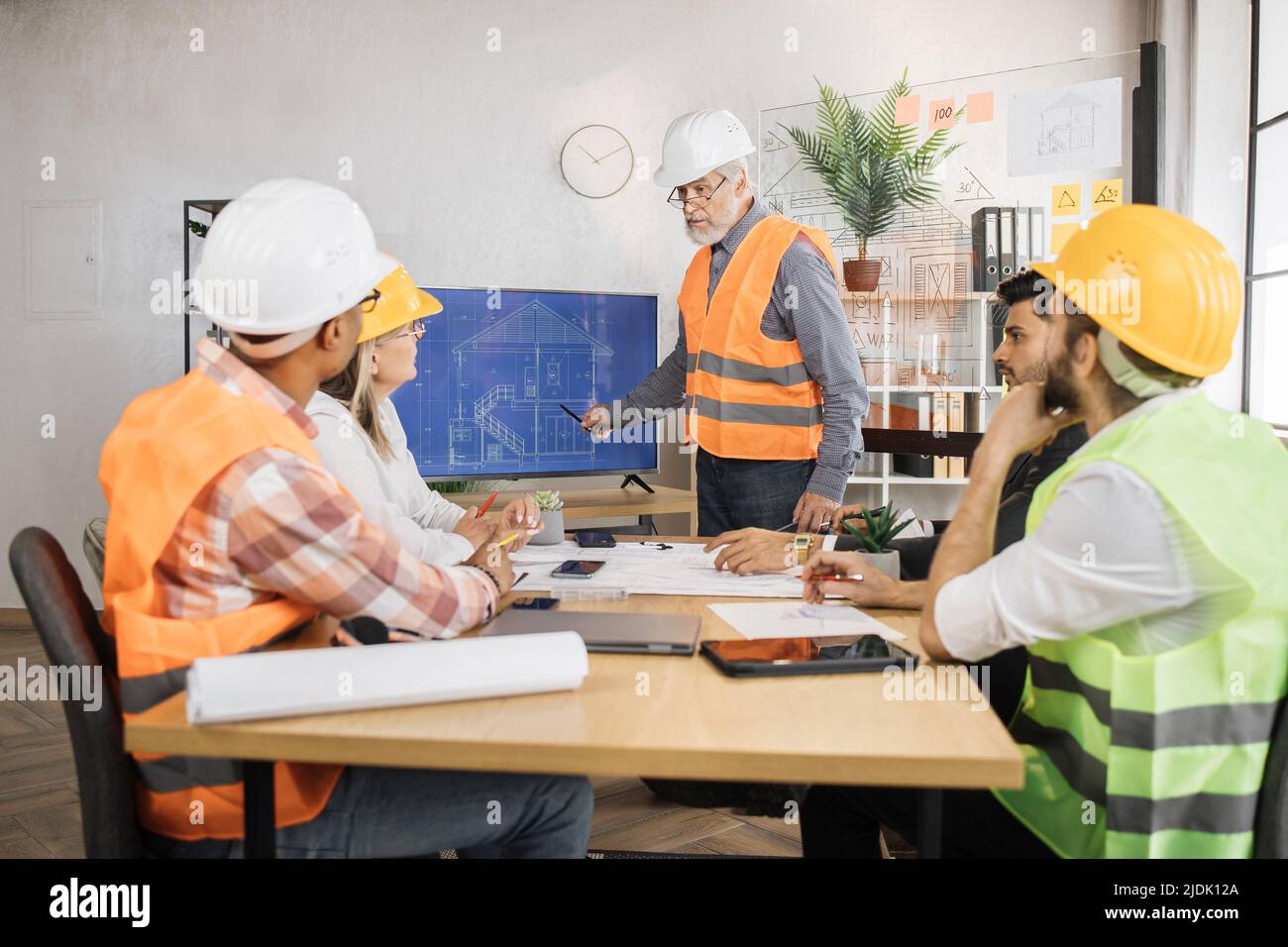 Senior bearded man in uniform and helmet presenting new construction ...