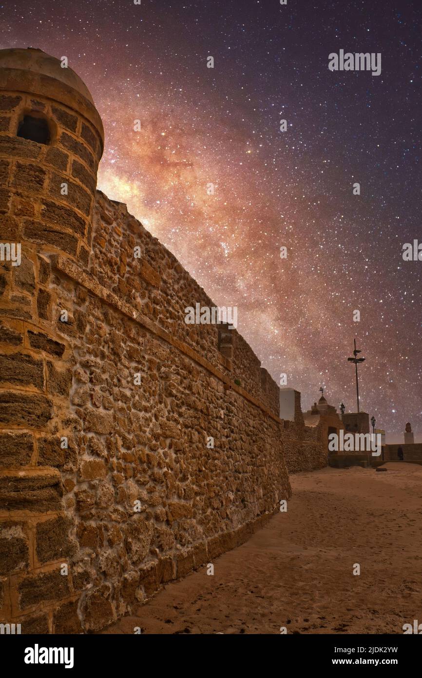 Night landscape with the Milky Way over the old stone walls of La Caleta beach in Cádiz, Spain Stock Photo