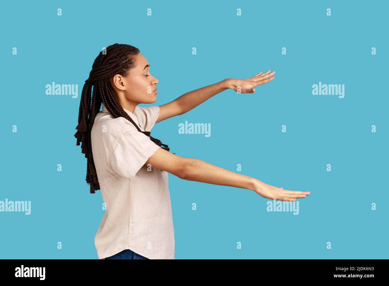 Side view of blind woman with outstretched hands walking alone with closed eyes in darkness, feels disoriented confused, lost road, wearing white shirt. Indoor studio shot isolated on blue background. Stock Photo
