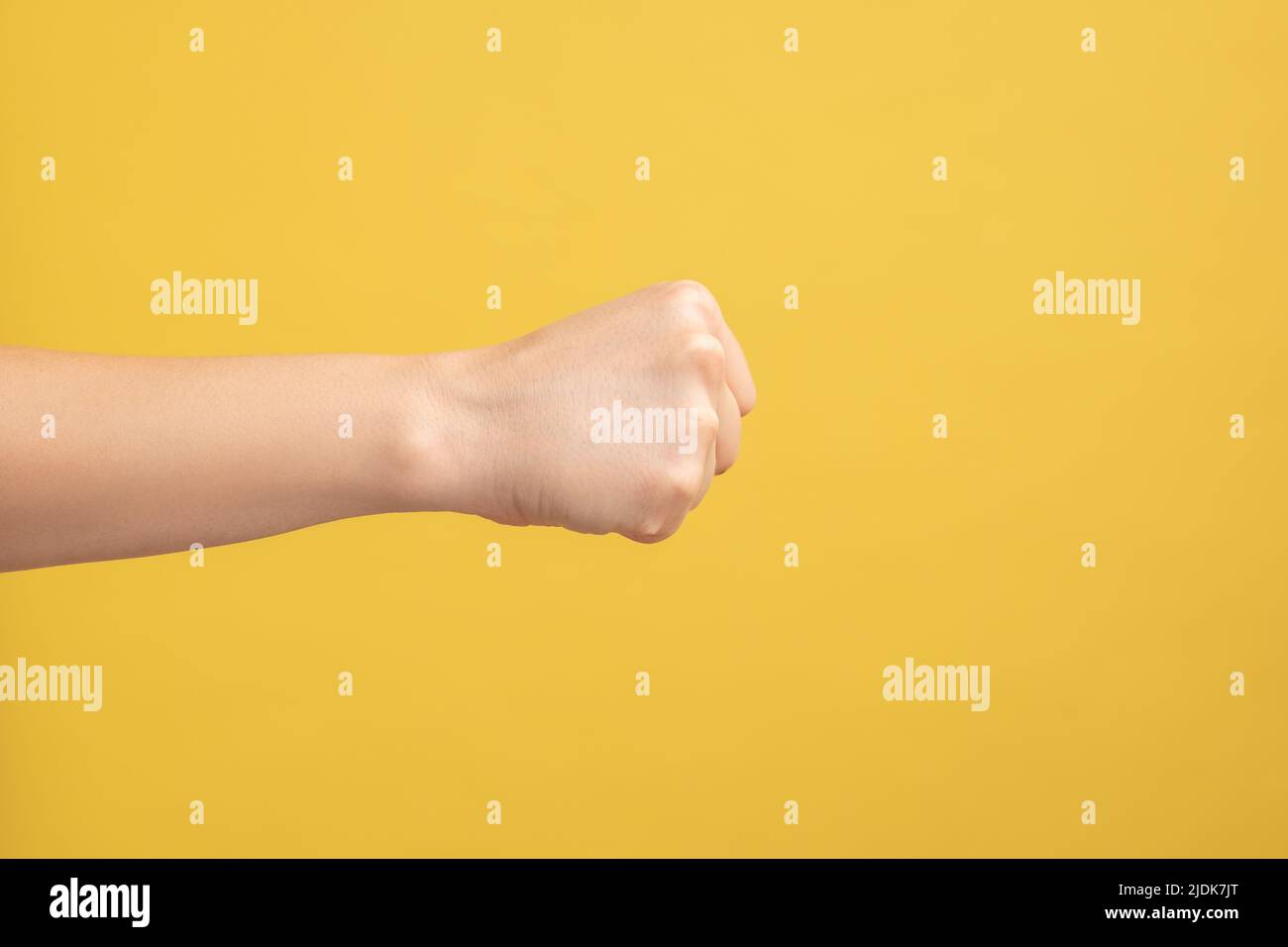 Profile side view closeup of woman hand showing boxing fists with hand, attack or defense against problems. Indoor studio shot isolated on yellow background. Stock Photo