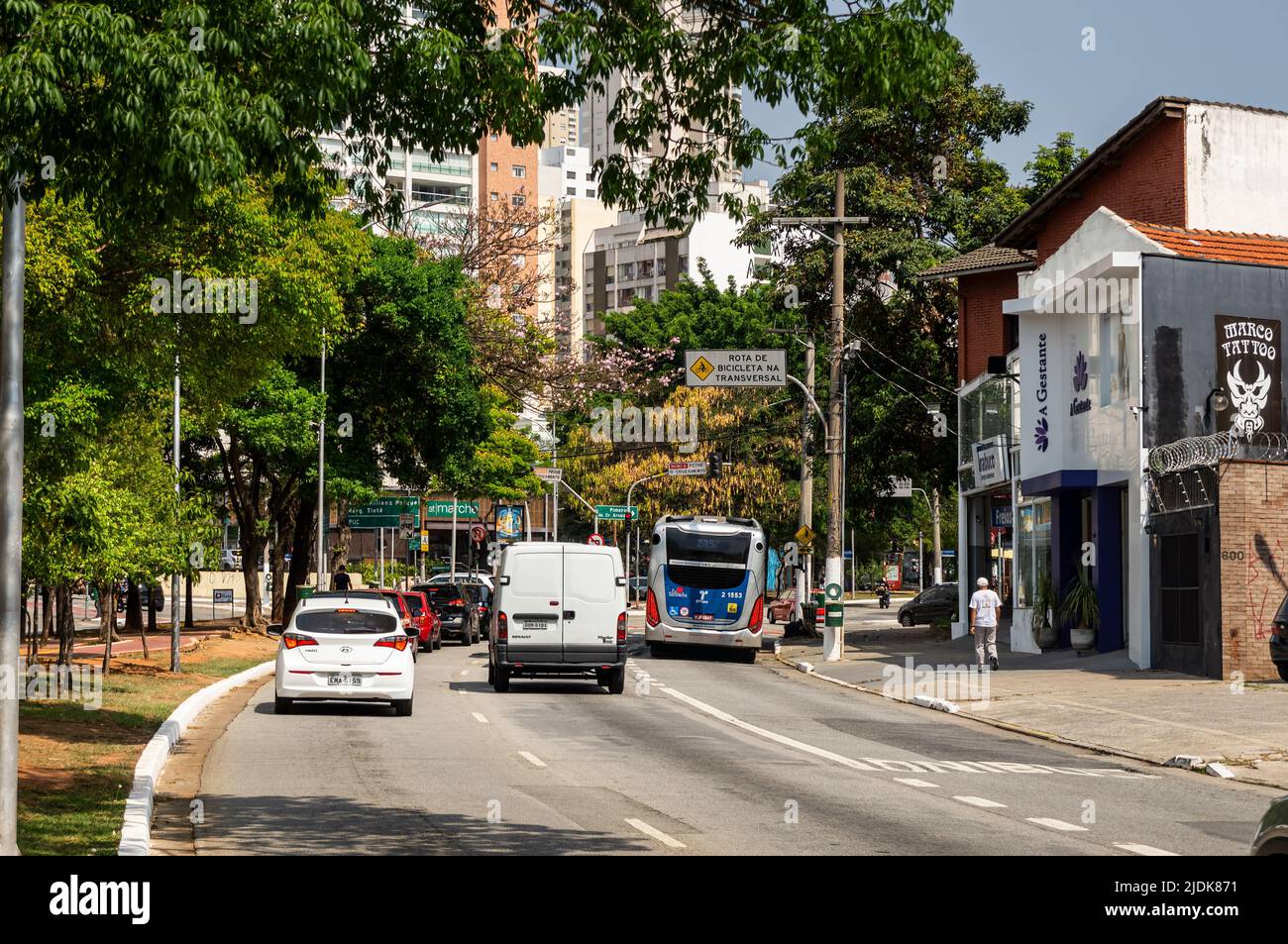 Cars passing by a curved section of Sumare avenue in Perdizes district area nearby small local shops in a normal business day under sunny blue sky. Stock Photo