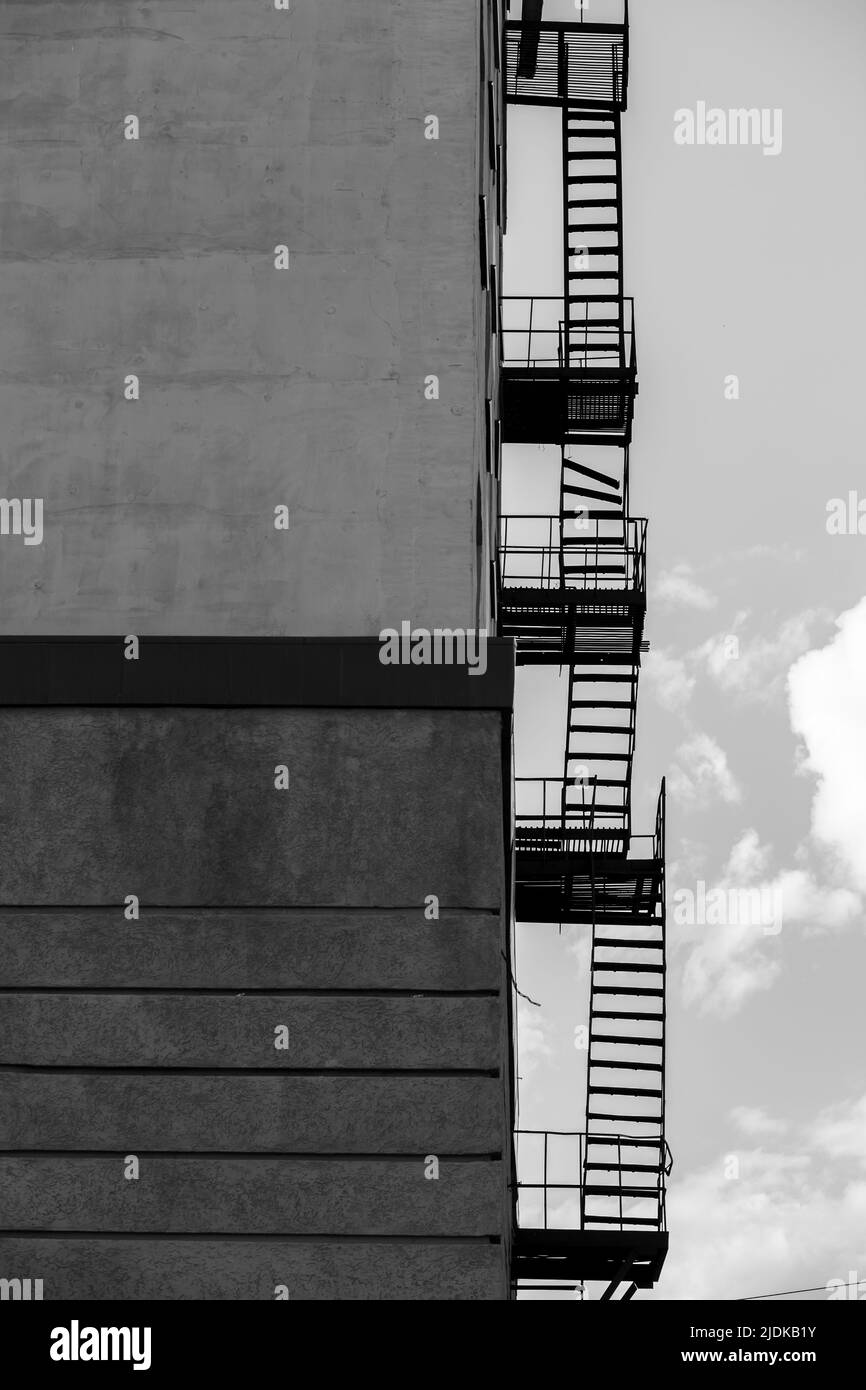 Silhouette of a fire escape on a high-rise building against a blue sky with clouds. Some of the stairs are broken. There is free space for text. Black Stock Photo