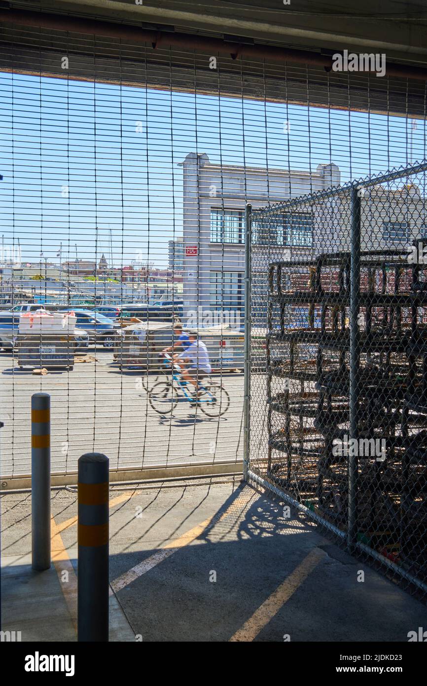 Crab pots stacked and stored indoors while two people cycle at Pier 45 in San Francisco, California. Stock Photo