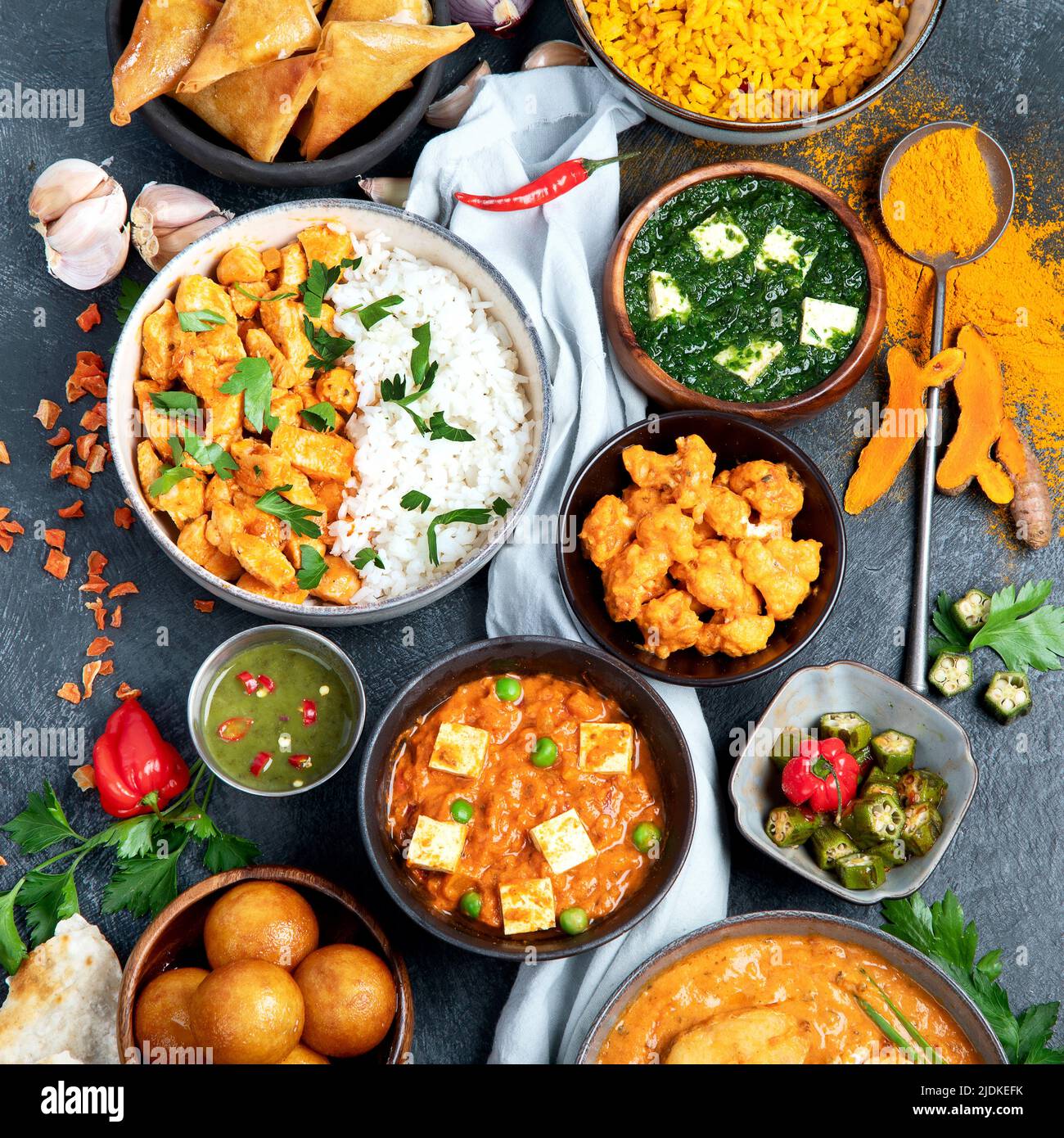 Dishes of indian cuisine. Curry, butter chicken, rice, lentils, paneer, samosa, spices. Bowls and plates with indian foodon dark on dark background. T Stock Photo