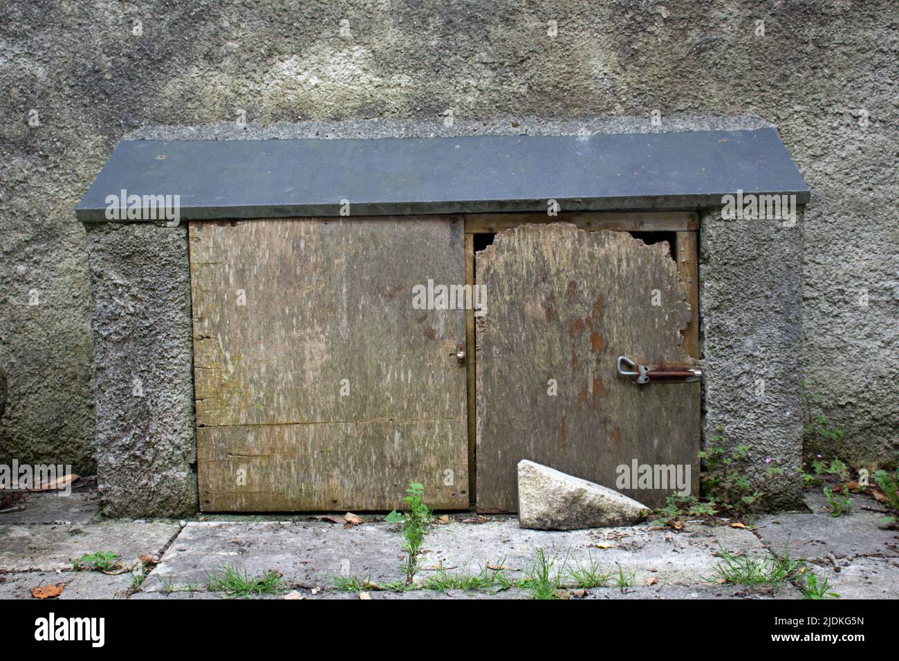 two low wooden doors in a cement cupboard with sloping roof and a grey wall behind Stock Photo