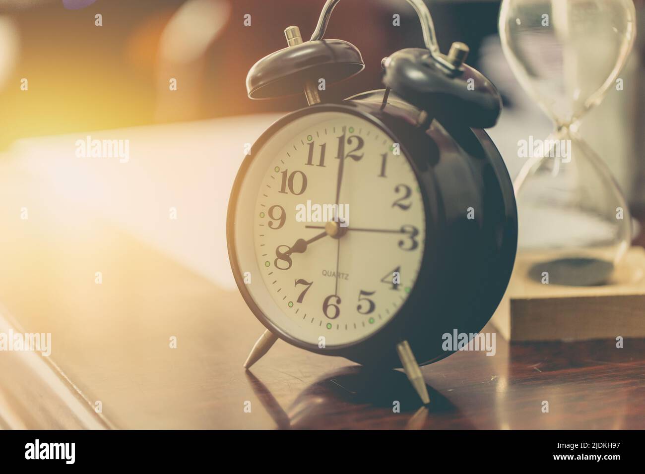 8 o'clock time retro clock with sand hourglass on wood table with sun ...