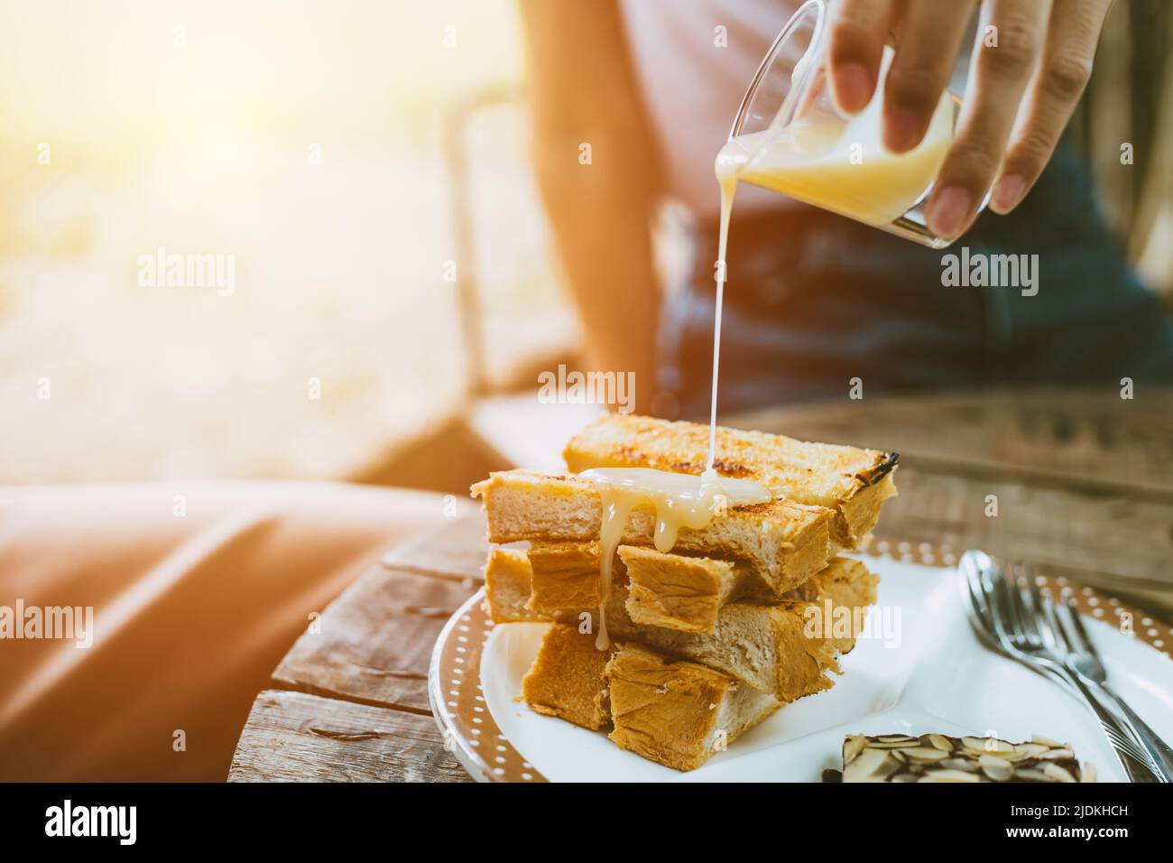 people pouring sweetened condensed milk on top of buttered toast enjoy eating fat and sweet menu in cafe. Stock Photo