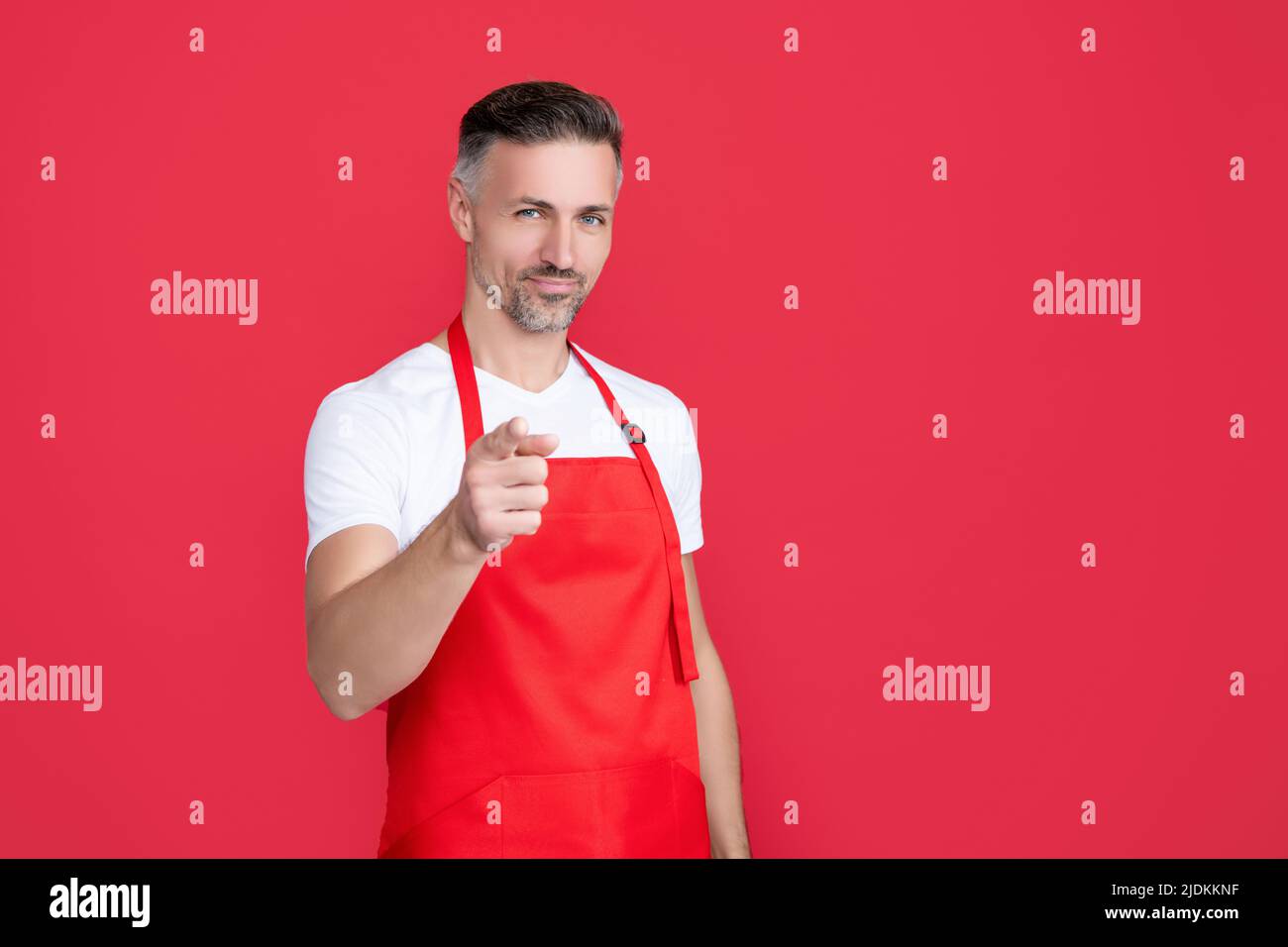 mature barman in apron on red background. point finger Stock Photo