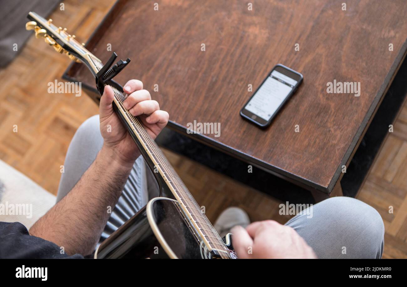 Amateur guitarist reading chords on mobile phone. Selective focus Stock Photo