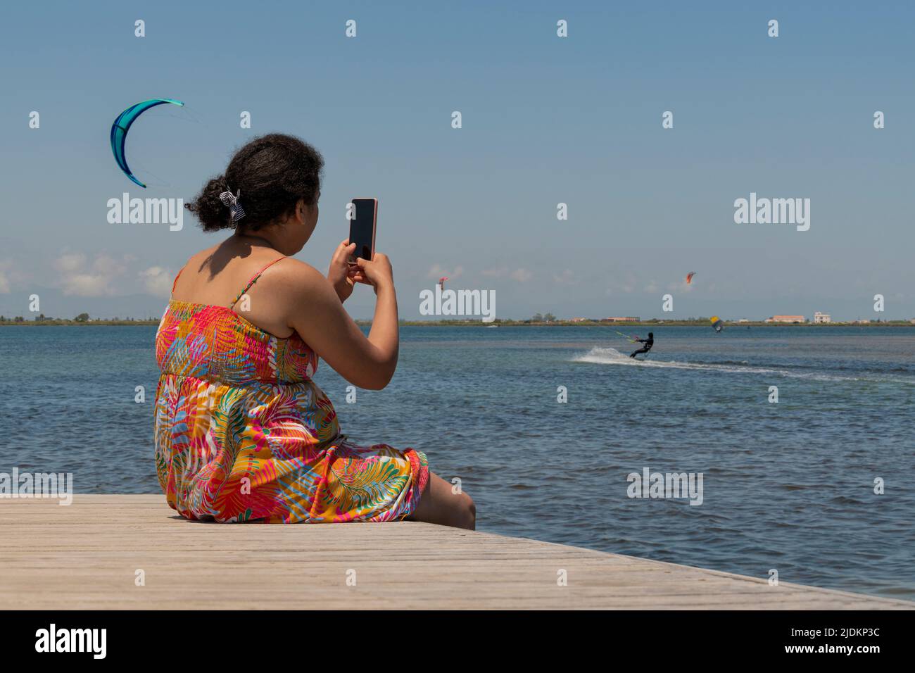 Sitting woman on a pontoon bridge with a kite surfer Stock Photo
