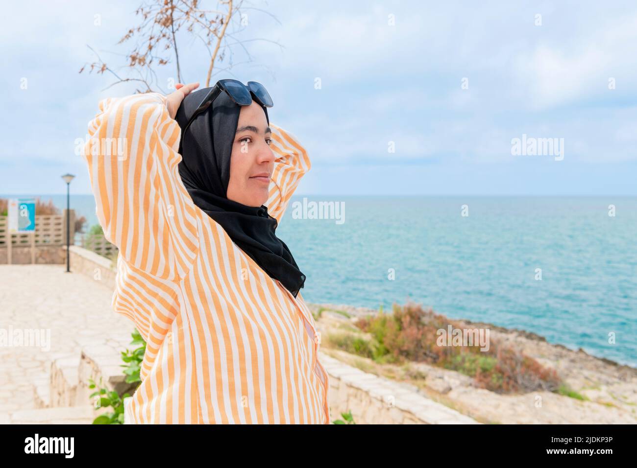 Maghrebi woman with hijab and glasses relaxing near the sea Stock Photo
