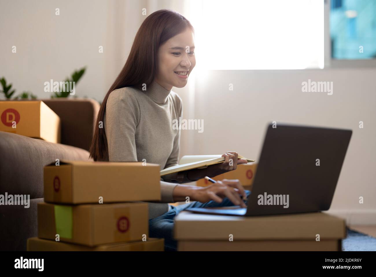 Asian woman Running Business From Home. Shipping shopping online, young start up small business owner packing cardboard box at workplace. Online Stock Photo