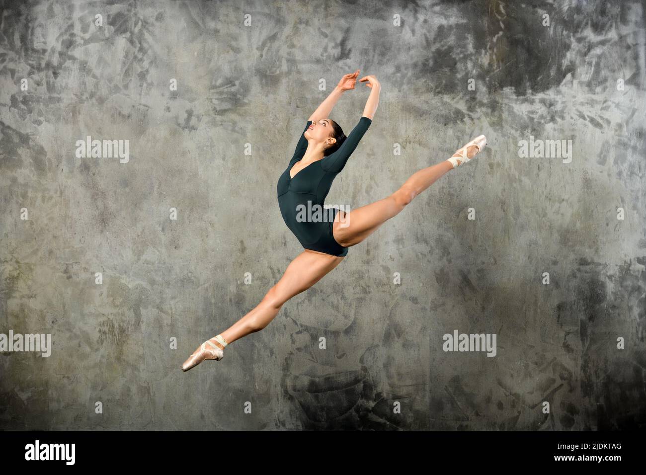 Graceful young ballerina leaping high in the air in a studio portrait against a grey wall with copyspace Stock Photo